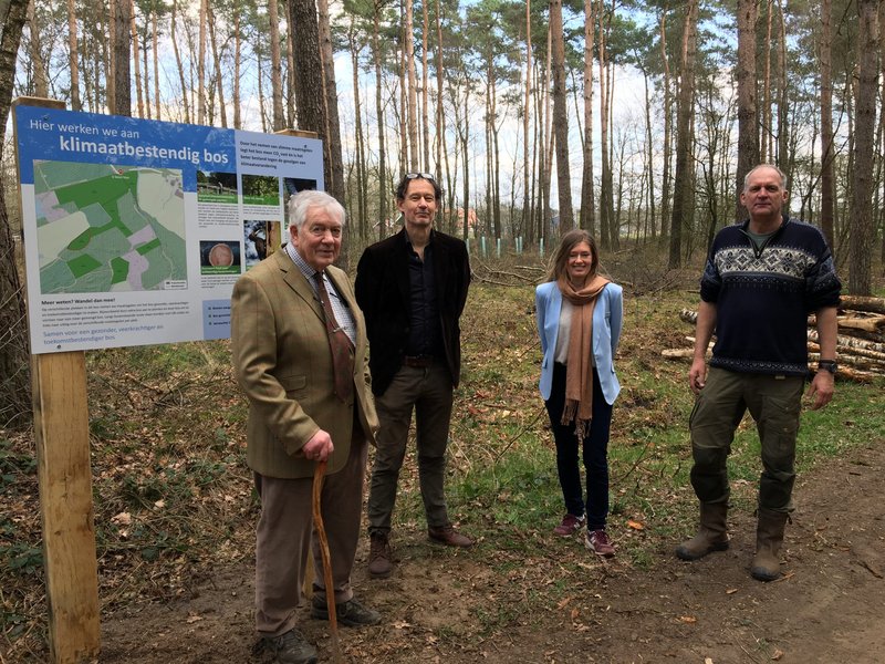 Vier personen voor een informatiebord in het bos.