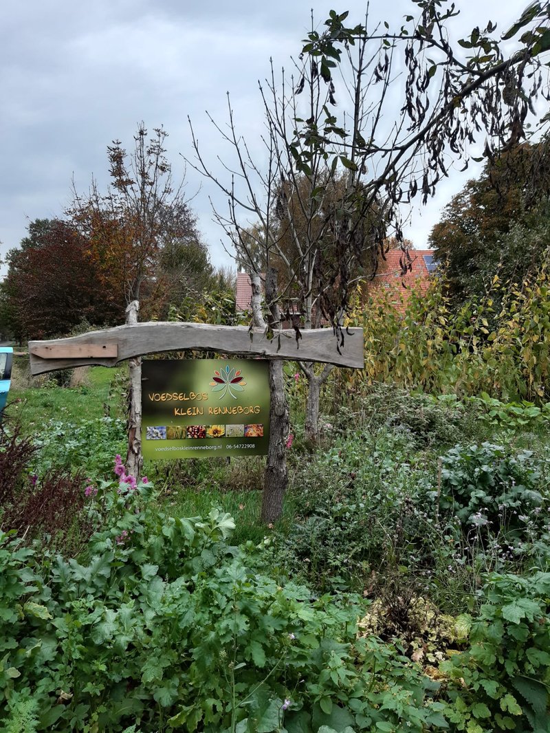 Welkomstbord in voedselbos tussen hoge en lage beplanting.